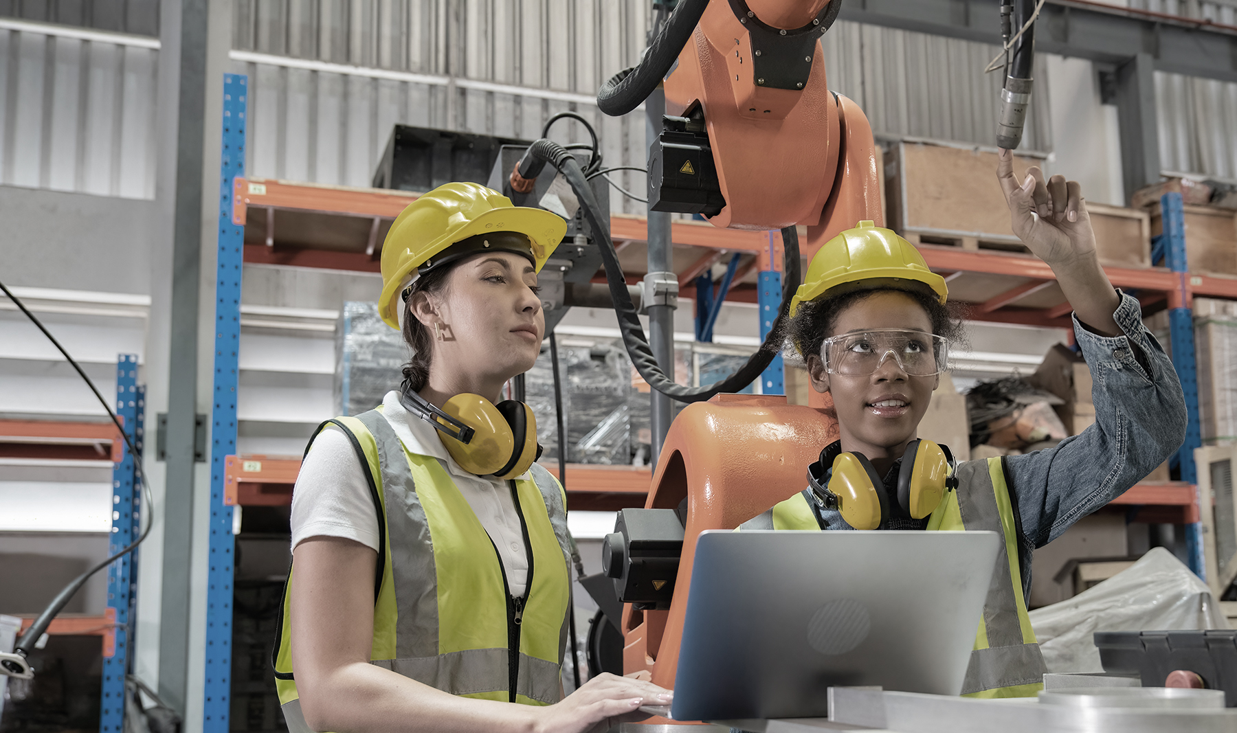Women Engineer wearing helmet and hi visible vest using laptop computer working in factory welding robotic automation happy smiling with quality control and programming pass
